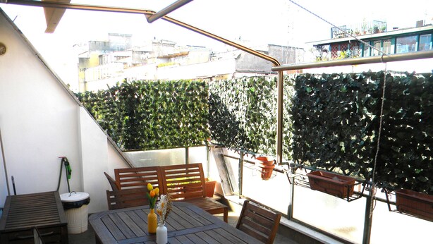 Un patio con una mesa y sillas de madera, una planta en maceta y una manguera.