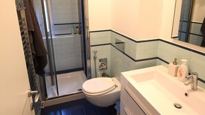Un baño moderno con cabina de ducha de vidrio, un lavabo blanco con espejo y un inodoro.
