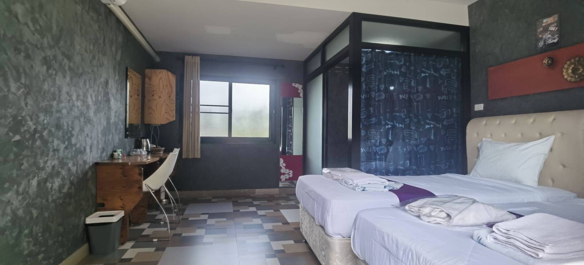 Une chambre à coucher avec un lit, un bureau et une chaise. Il y a une fenêtre avec des rideaux, une horloge murale et une porte avec un rideau à motifs.