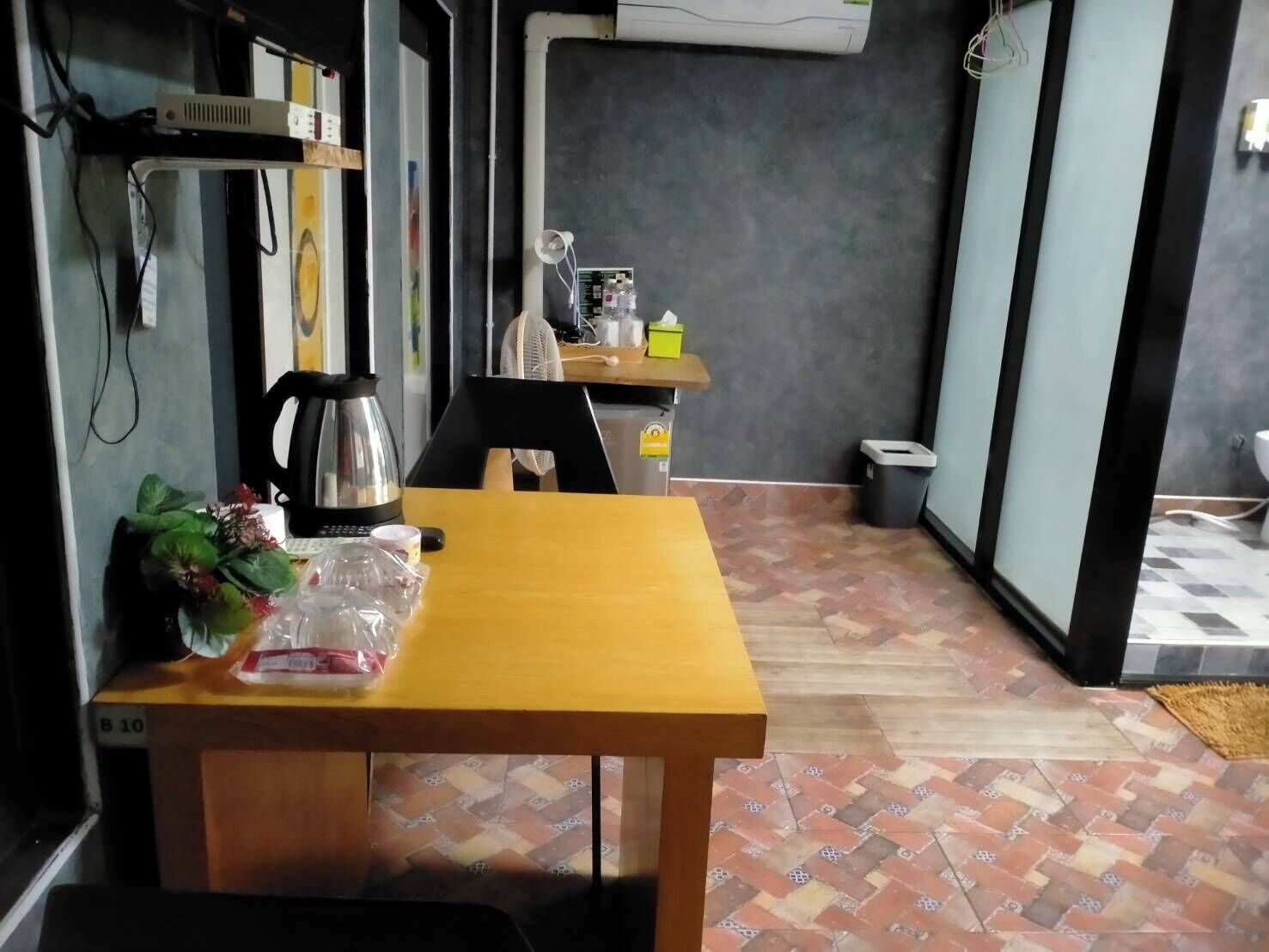 A small dining area with a wooden table, chairs, a kettle, and a fan.