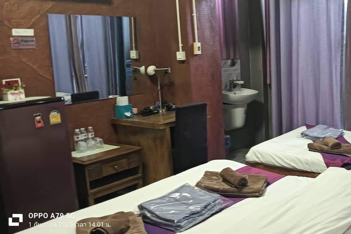 A hotel room with two beds, a desk with a lamp, a sink, and a mirror.