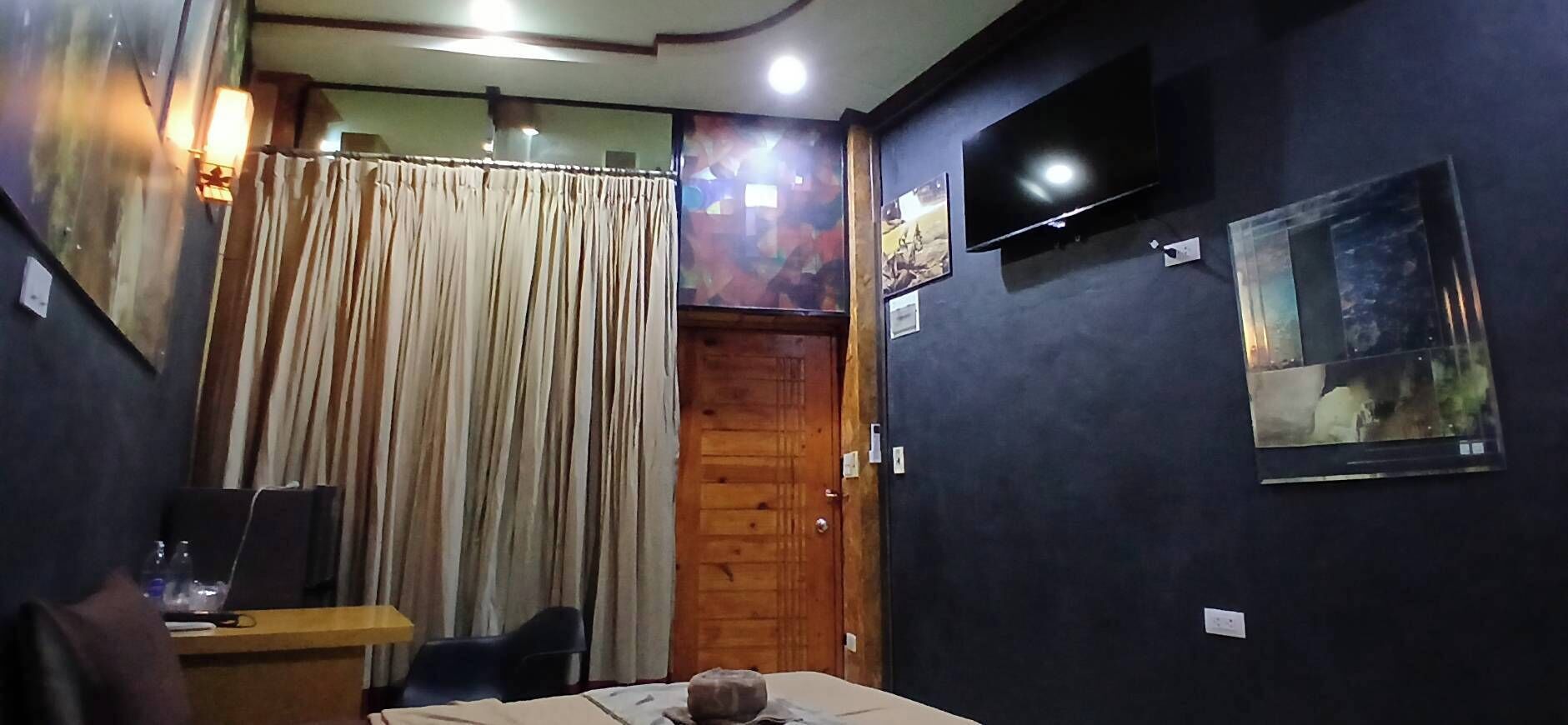 Habitación de hotel con cama, escritorio con laptop, televisor montado en la pared y cortina.