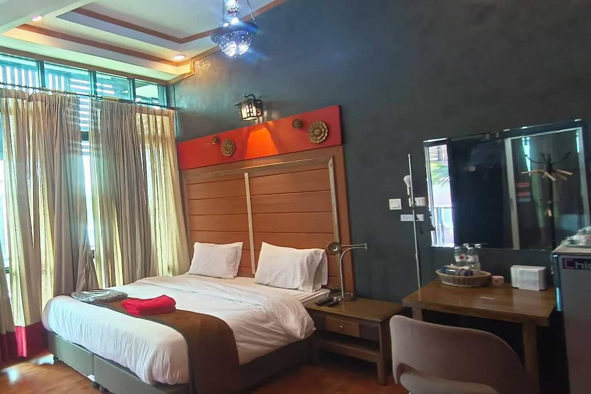 A hotel room with a bed, a desk, a chair, a mirror, and curtains.