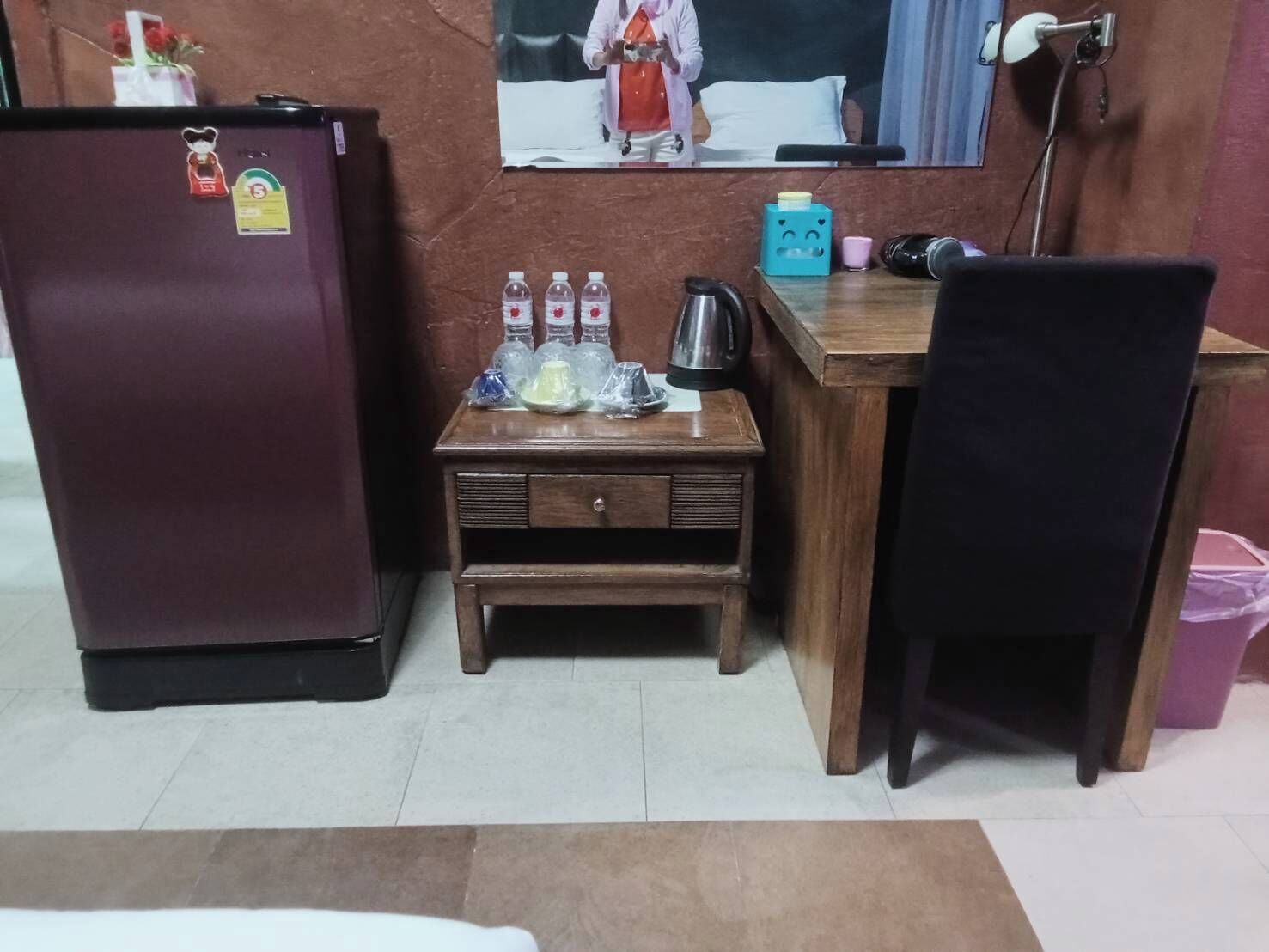 Une petite pièce comprenant un réfrigérateur, une petite table en bois avec des bouteilles, une bouilloire et une chaise.