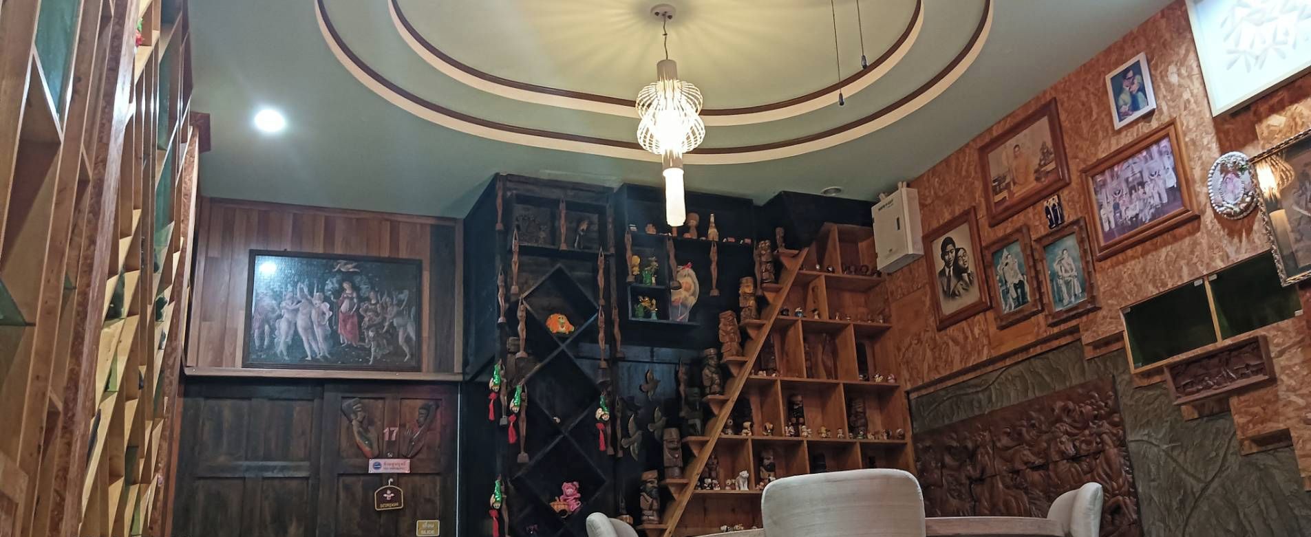 A room with a wooden staircase, a chandelier, and shelves with various items.