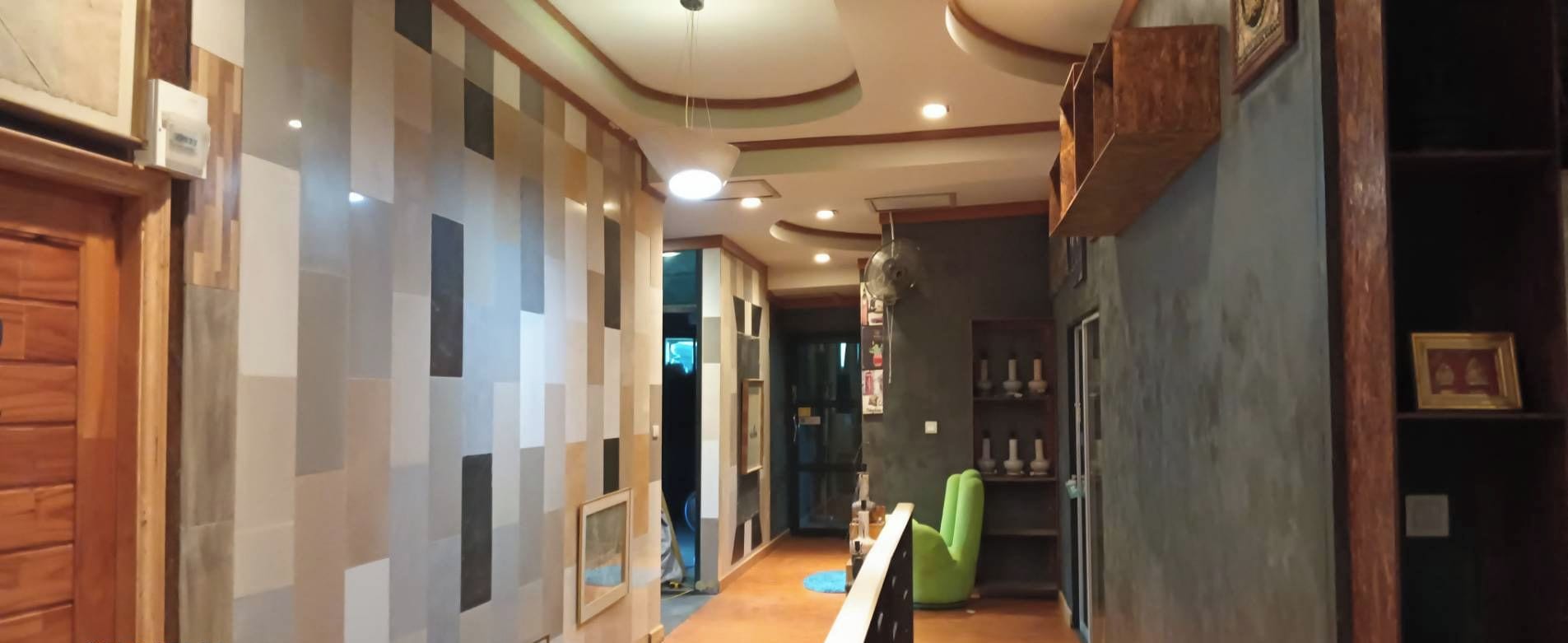 A hallway with a wooden door on the left, a checkered wall pattern, and a green chair in the center.