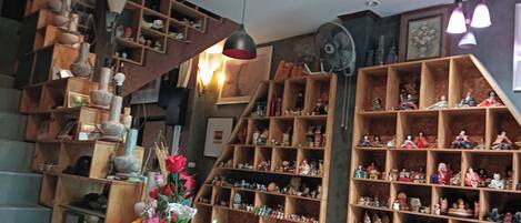 A room with wooden shelves filled with various items, a staircase, and a fan.