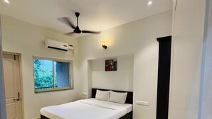 A modern bedroom with a bed, ceiling fan, air conditioning unit, and a window with a view of greenery. - Raj Exotic Palms (Vagator)