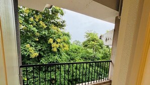 A balcony with a metal railing, a tiled floor, and a view of lush greenery and trees. - Raj Exotic Palms (Vagator)
