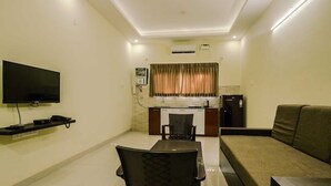 A compact living space with a dining area, a sofa, a TV, and a kitchenette. - Raj Exotic Palms (Vagator)
