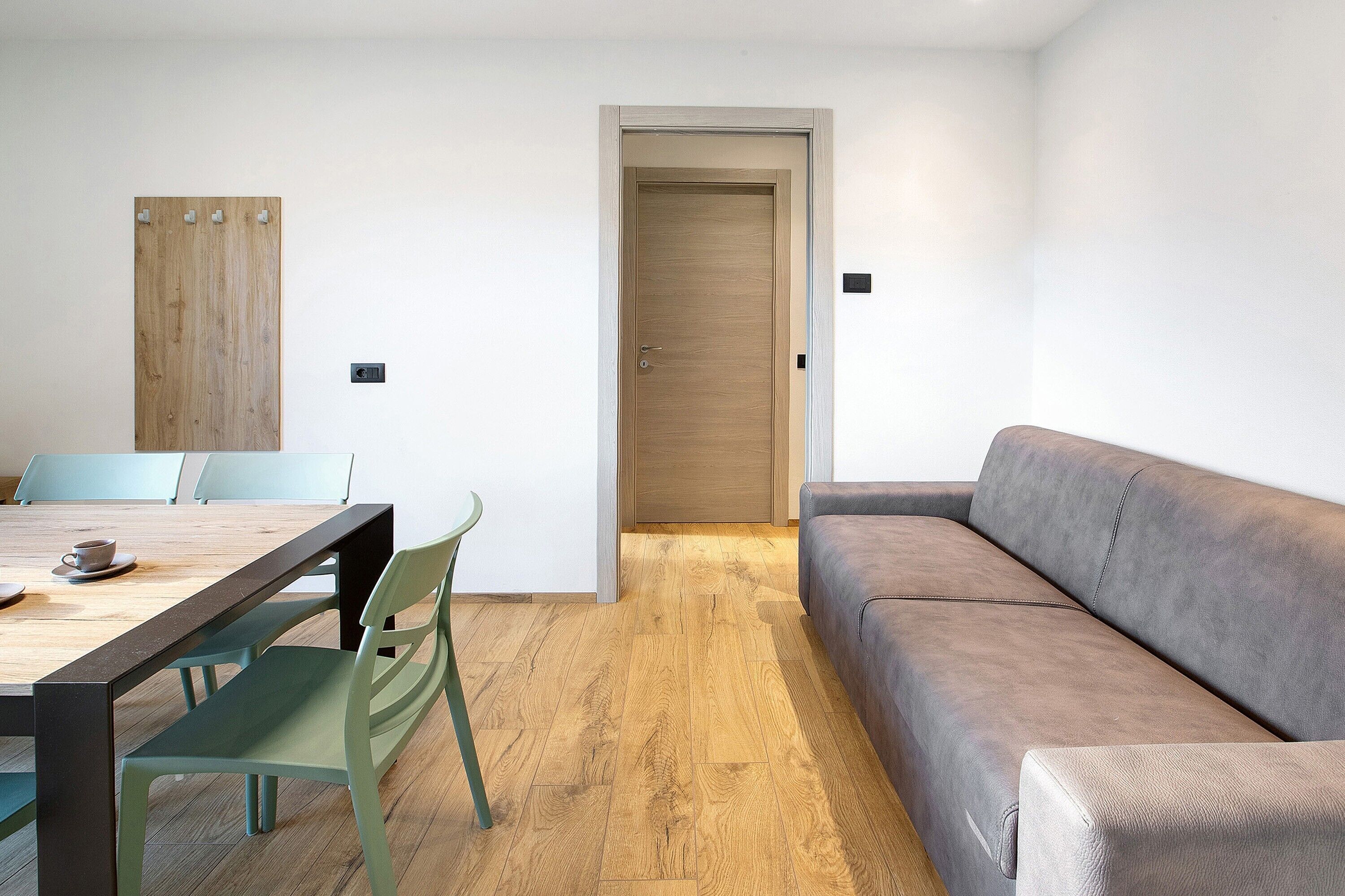 Una habitación con piso de madera, un sofá, una mesa de comedor con sillas y una puerta.