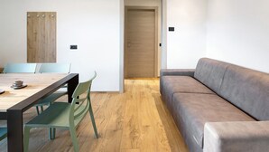 A room with a wooden floor, a sofa, a dining table with chairs, and a door. - Apartment '3' with Mountain View, Shared Garden and Wi-Fi (Valdidentro)