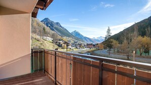 A balcony with a wooden railing overlooking a mountainous landscape with buildings and a river. - Apartment '3' with Mountain View, Shared Garden and Wi-Fi (Valdidentro)