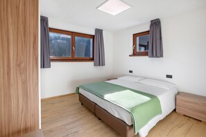 Una camera da letto con un letto, due finestre con tende, un comodino e un tavolino.
