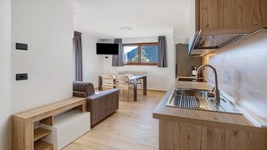 Une cuisine de taille réduite, équipée d’un évier, de meubles en bois et d’un coin repas avec une table et des chaises.