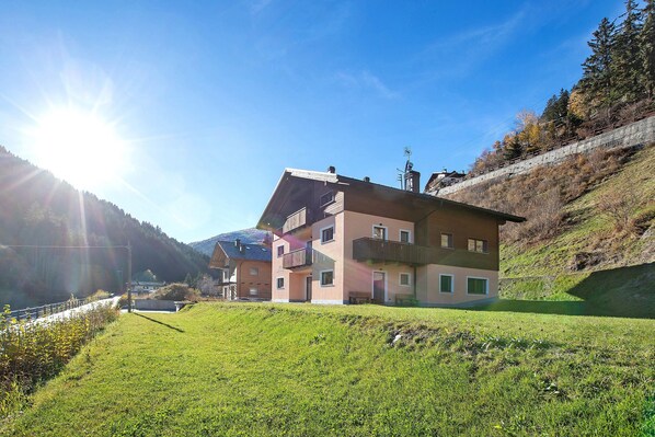 A multi-story building with balconies, situated on a hillside with a clear sky and sunlight.