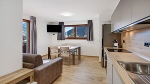 Une cuisine compacte avec un coin repas, un canapé et un téléviseur fixé au mur.