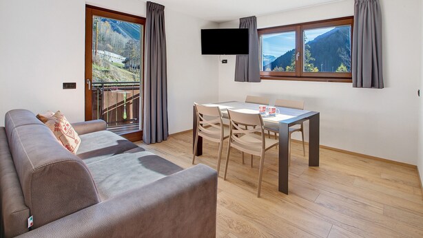 Une pièce moderne comprenant un canapé, une table à manger, des chaises, un téléviseur et de grandes fenêtres avec des rideaux.