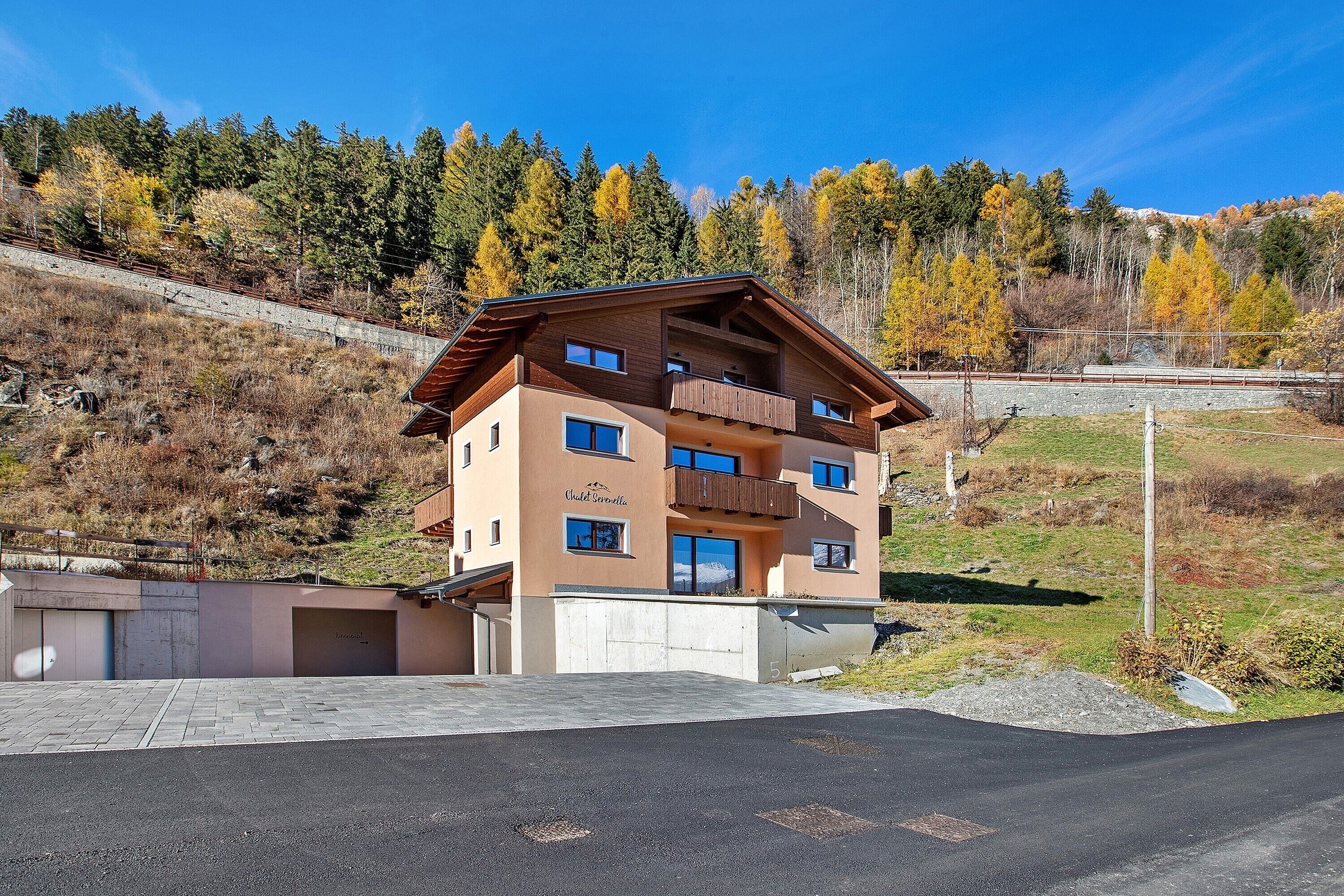 A multi-story hotel with a balcony on the second floor, a garage, and a view of a forested hillside.