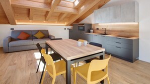 Et moderne køkken med ovenlys, et spiseområde med et træbord og gule stole, samt en grå sofa med farverige puder.