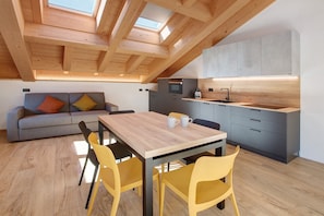 Una cocina moderna con tragaluz, comedor con mesa de madera y sillas amarillas, y sofá gris con cojines de colores.