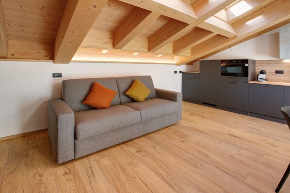 A modern kitchen with a built-in oven and a grey sofa with two cushions.