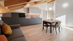 Et moderne køkken med spiseplads, træbjælker i loftet og en gr å sofa.