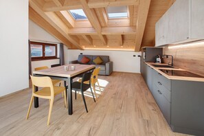 Una cocina moderna con tragaluz, vigas de techo de madera, un comedor con mesa y sillas, y un armario gris.