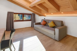 Una habitación con techo de madera, un sofá con cojines, una mesa de comedor con sillas y una ventana con cortinas.