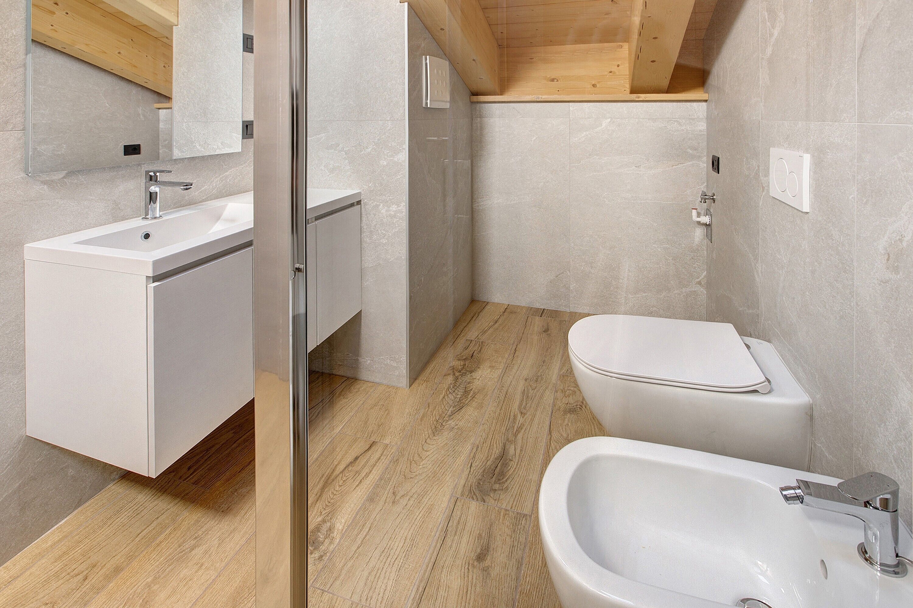 A modern bathroom with a wooden ceiling, a white sink, a toilet, and a bidet.