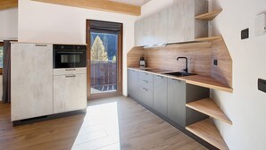A modern kitchen with built-in appliances, wooden shelves, and a sliding glass door leading to a balcony. - Apartment '6' with Mountain View, Shared Garden and Wi-Fi (Valdidentro)