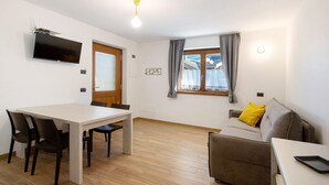 A modern living room with a dining table, sofa, and TV. - Apartment '1' with Mountain View, Shared Terrace and Wi-Fi (Isolaccia)