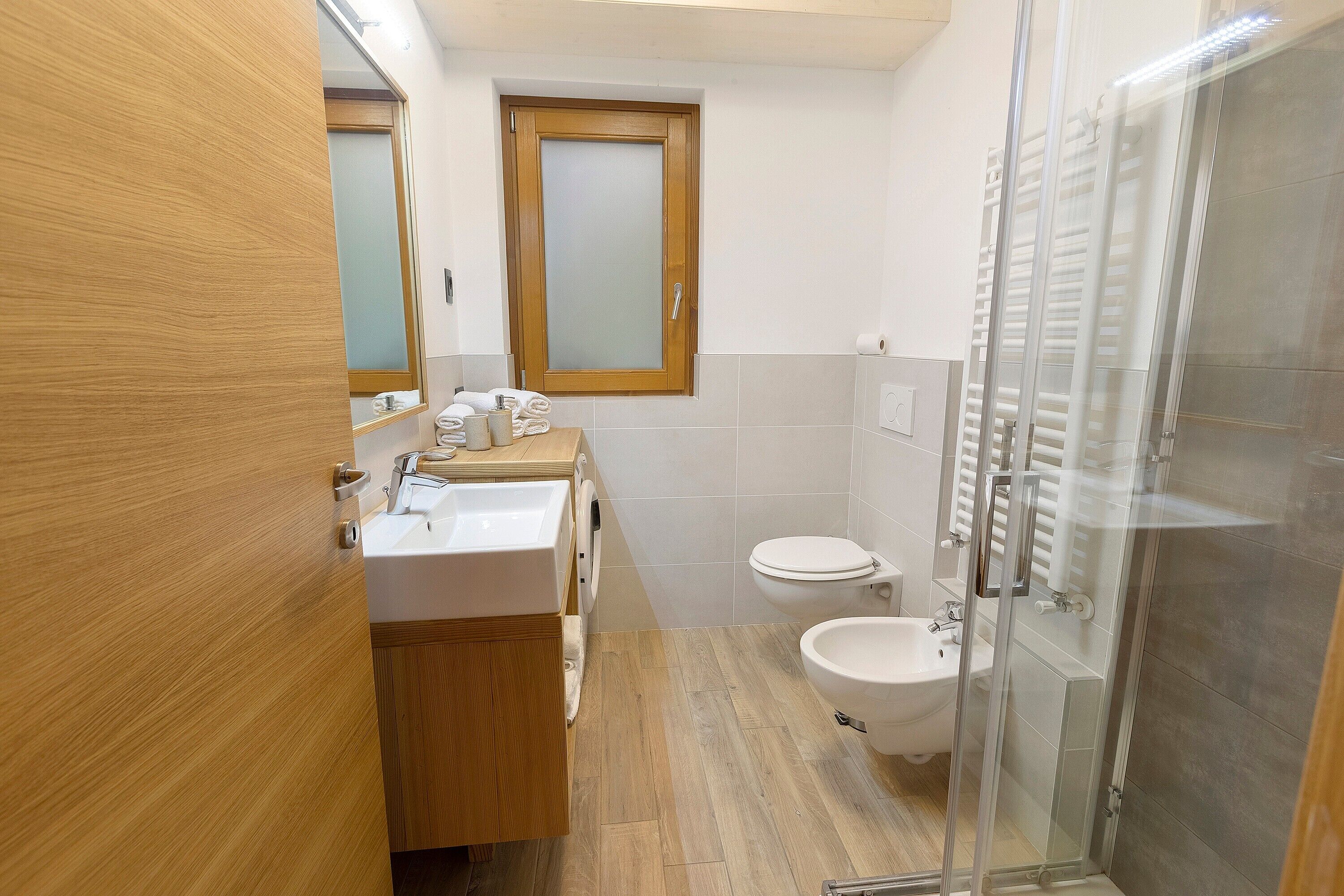 Un bagno con un mobile vanitario in legno, un water, un bidet e una cabina doccia in vetro.