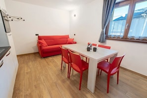 A compact living space with a kitchenette, a dining area with red chairs, a red sofa, and a window with a view.