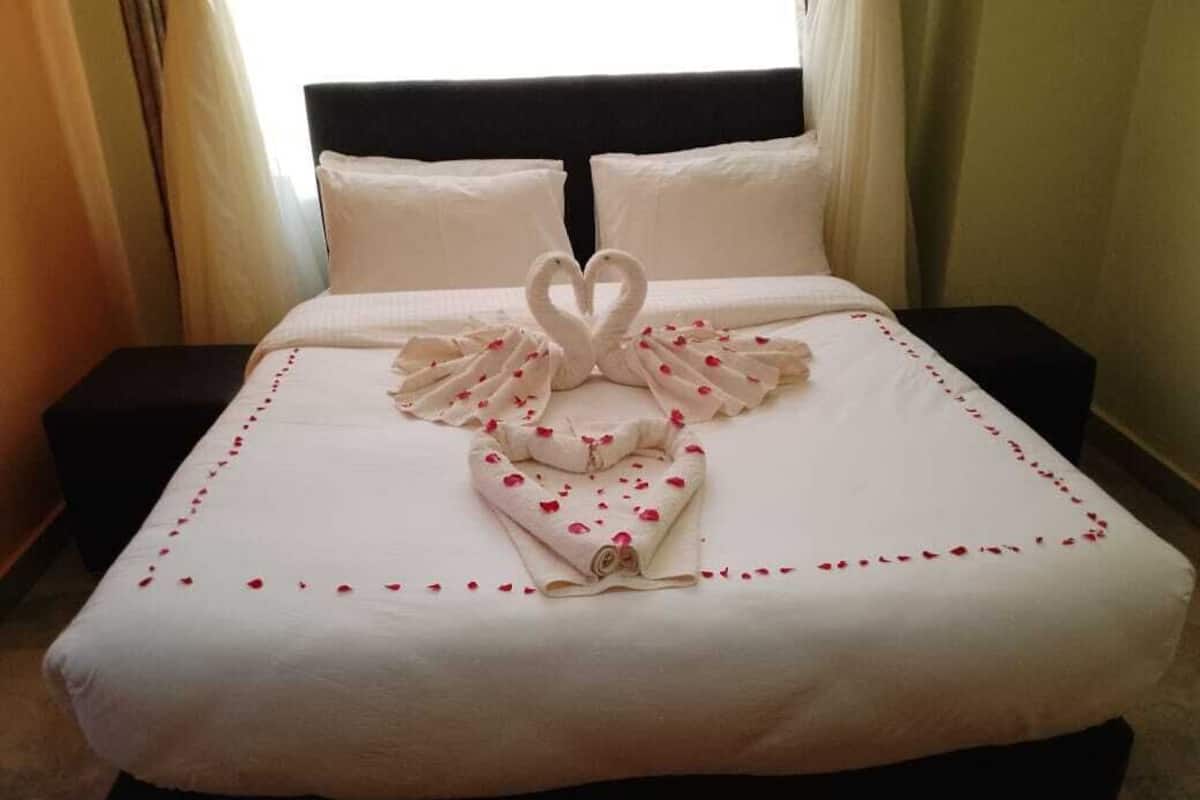 A neatly made bed with a heart-shaped towel arrangement and rose petals.