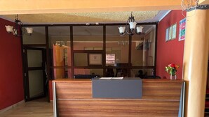 A reception area with a wooden reception desk, a glass door entrance, and a chandelier. - The Victorian Hotel Marsabit (Marsabit)