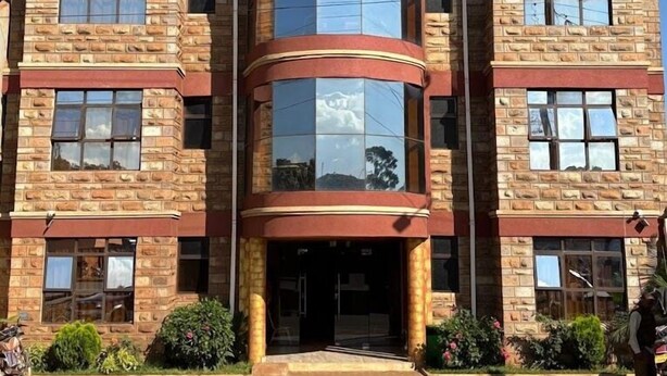 A multi-story building with a central glass tower, stone facade, and a symmetrical design. - The Victorian Hotel Marsabit (Marsabit)