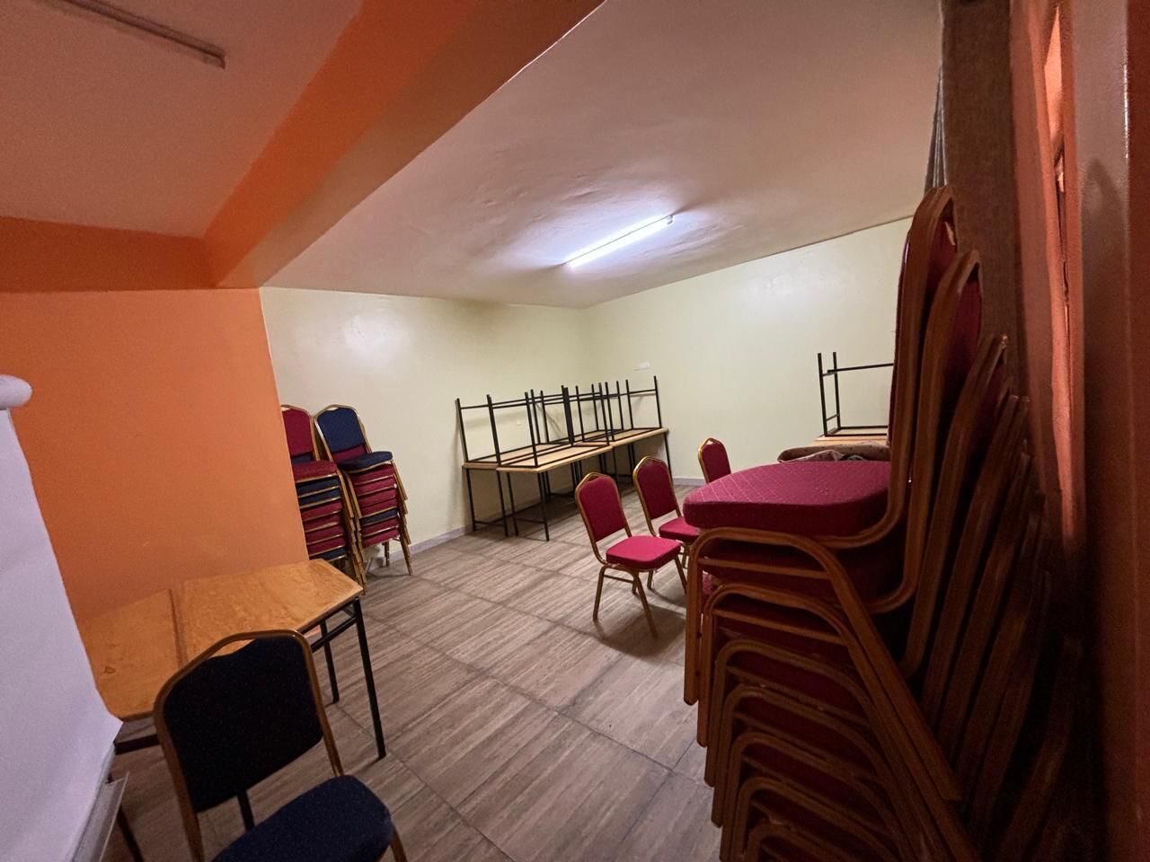 A room with a long table and chairs, a bench, and a stack of chairs against the wall.