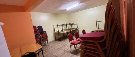 A room with a long table and chairs, a bench, and a stack of chairs against the wall.