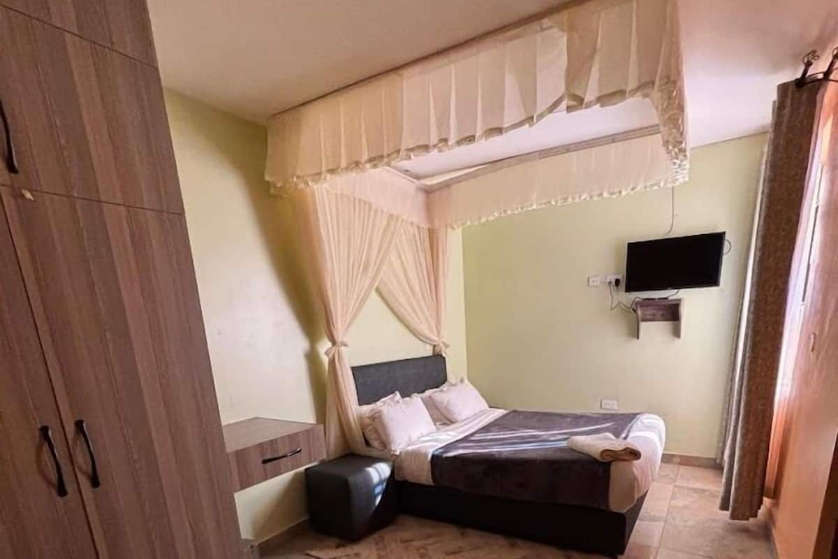 A bedroom with a bed, a nightstand, a chair, a TV, and a wardrobe.