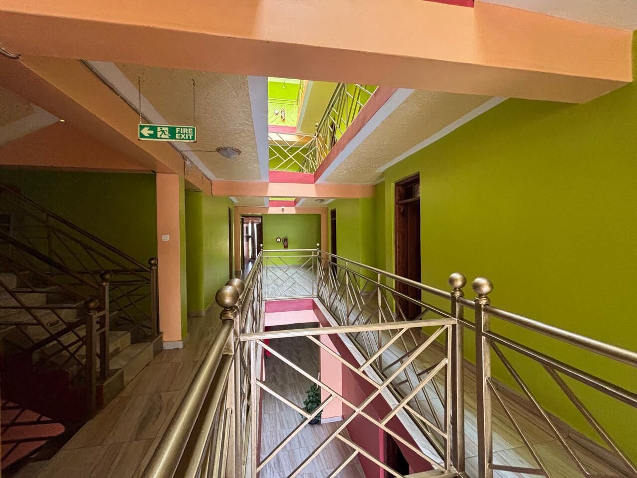 A multi-level corridor with a fire exit sign, metal railings, and a staircase.