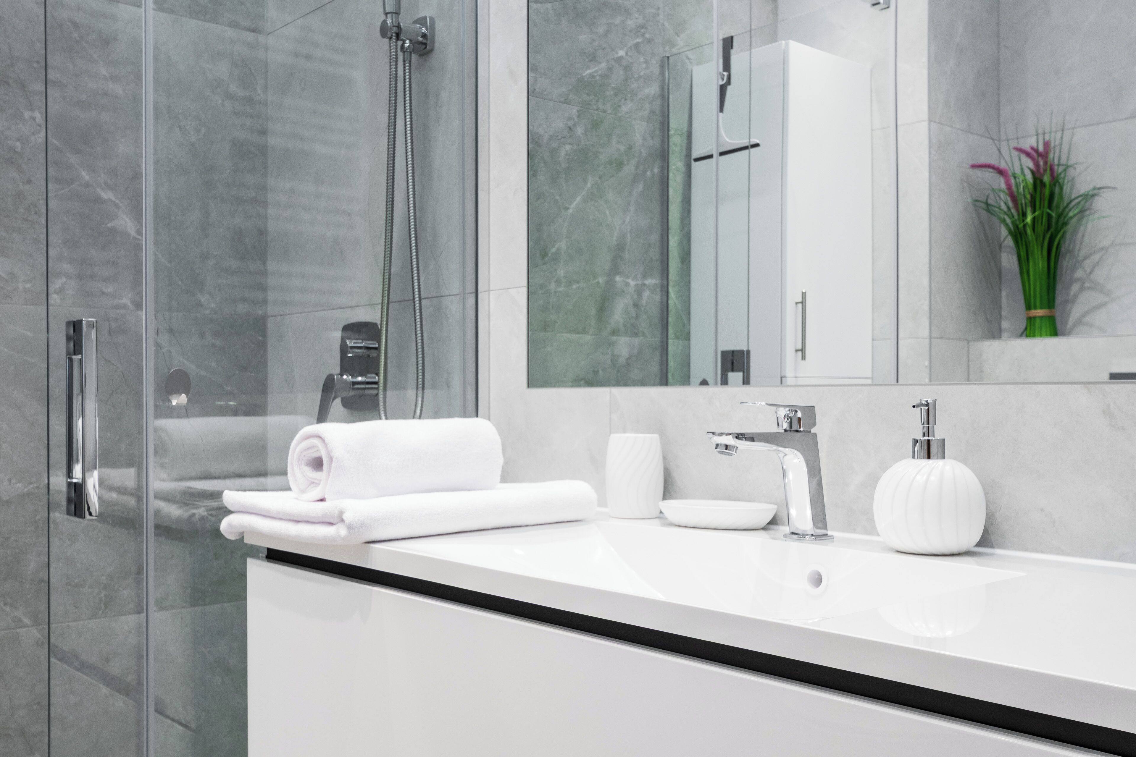 A modern bathroom with a glass shower enclosure, a white sink with a black countertop, and a mirror above the sink.