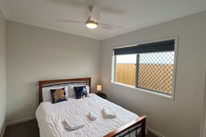Un dormitorio con cama, ventilador de techo, ventana con vistas y mesita de noche con lámpara.
