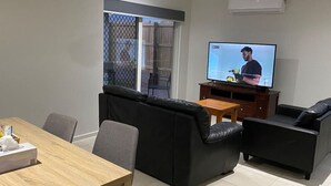 Ein Wohnzimmer mit Fernseher, Sofa und Esstisch.