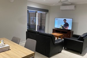 Una sala de estar con televisor, sofá y mesa de comedor.