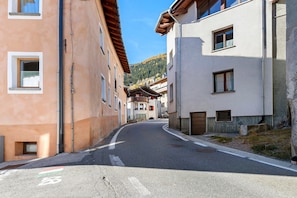 A narrow street with buildings on either side, a clear sky, and a mountain in the background.