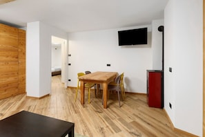 A room with a wooden dining table, chairs, a TV mounted on the wall, and a red appliance.