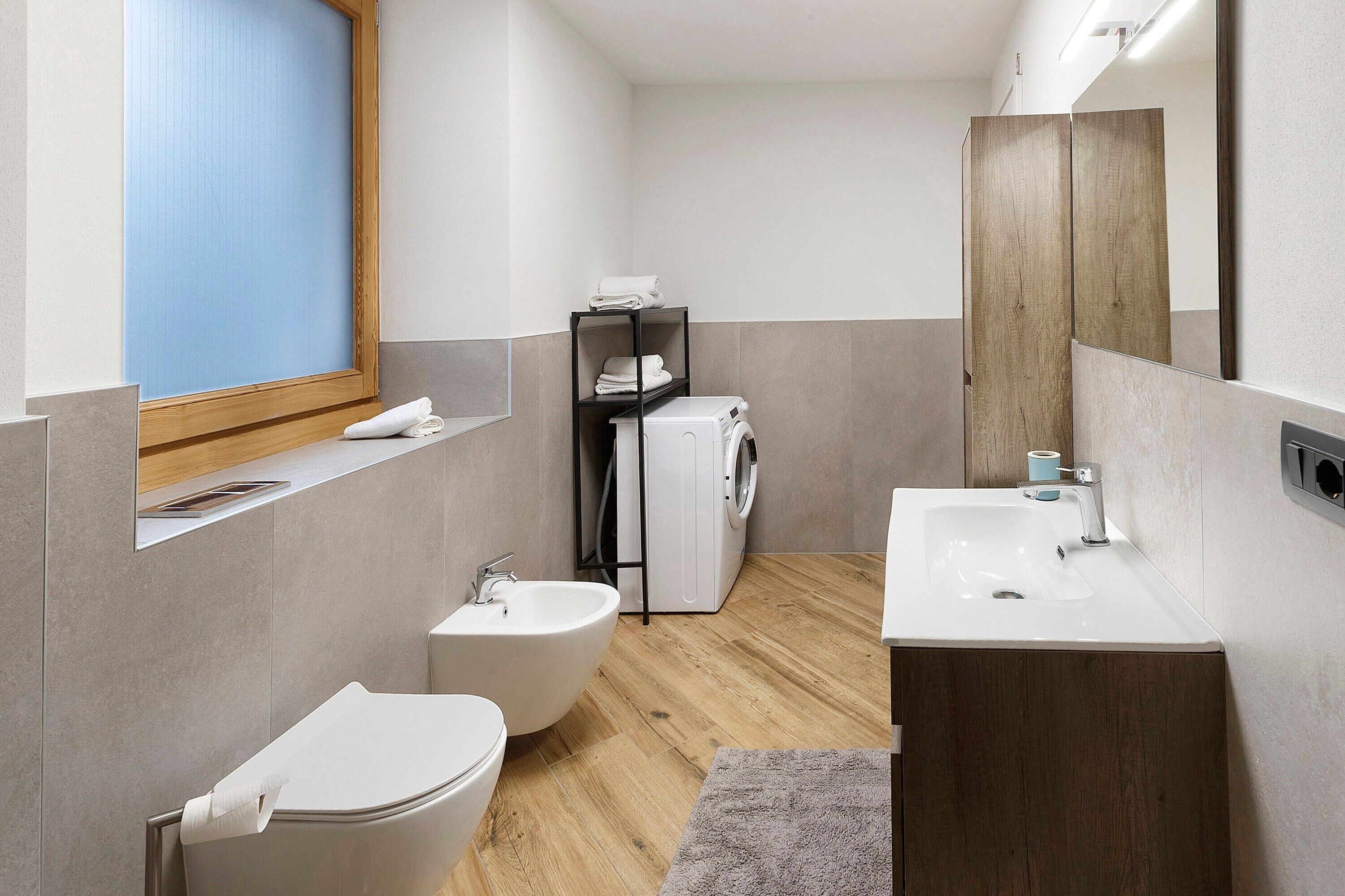Een moderne badkamer met een hygiëneschuimer, een wastafel, een spiegel, een handdoekhouder en een wasmachine.