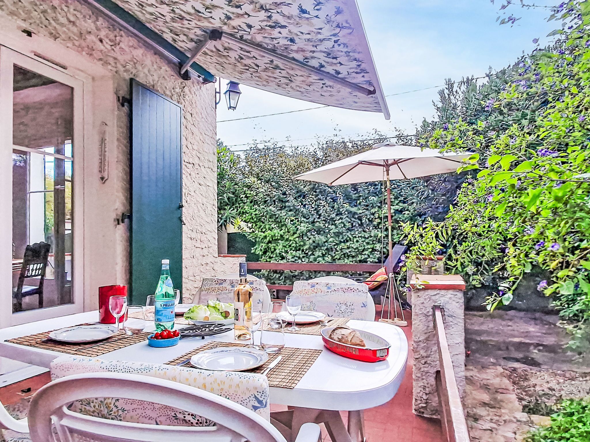 An outdoor dining area with a table set for two, a bottle of water, and a bowl of fruit.