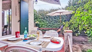An outdoor dining area with a table set for two, a bottle of water, and a bowl of fruit.